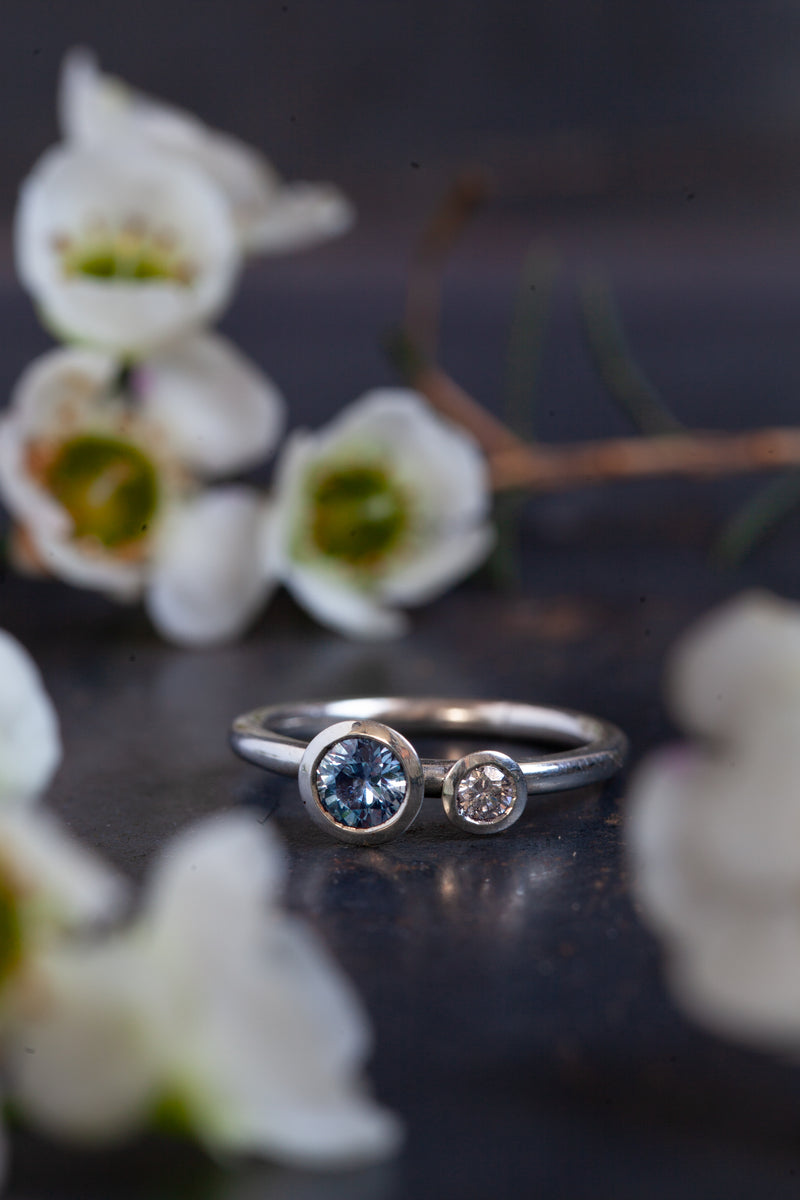 An exquisite Sapphire in a white gold cup setting, beautifully paired with a sophisticated grey diamond, sitting on an 18ct white gold band